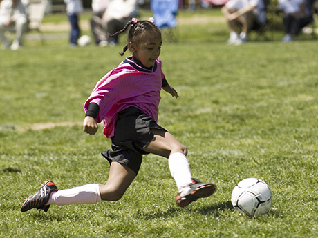 Young African American soccer player kicking the ball.